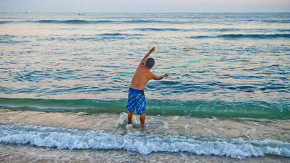 Pescador arroja su red a una ola en la playa